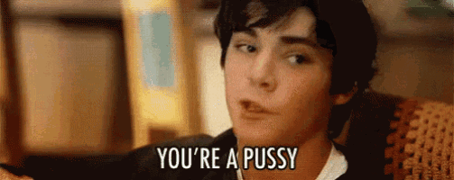 a young man is sitting on a couch and says you 're a pussy .