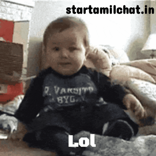 a baby wearing a varsity shirt sits on a bed
