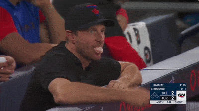 a man sitting in a dugout watching a baseball game with a scoreboard that says cle 2 tor 2