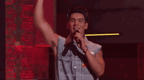 a man in a denim vest is singing into a microphone .