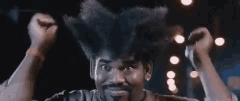 a man with a beard and a very large afro is holding his fist in the air .