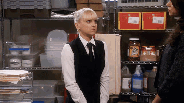 a woman in a black vest and tie stands in front of a shelf that has a few boxes on it that say llc