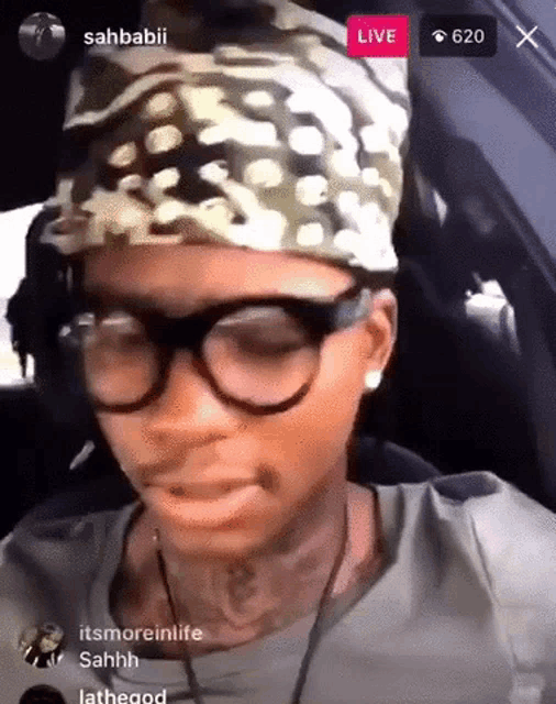 a woman wearing glasses and a headband is sitting in a car with a live button in the corner