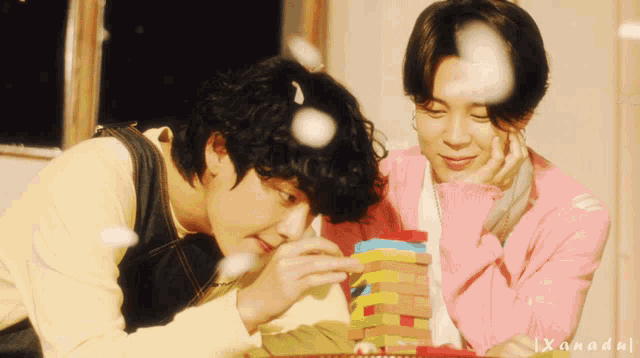 two young men are playing with a stack of blocks and the name xanadu is on the bottom left