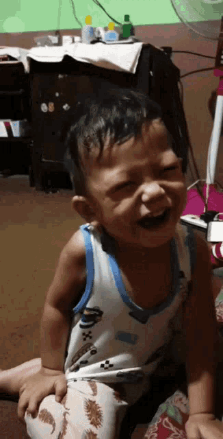 a little boy is sitting on the floor laughing with his eyes closed