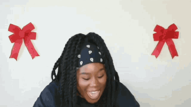a woman with dreadlocks is wearing a headband and smiling in front of a wall with red bows .