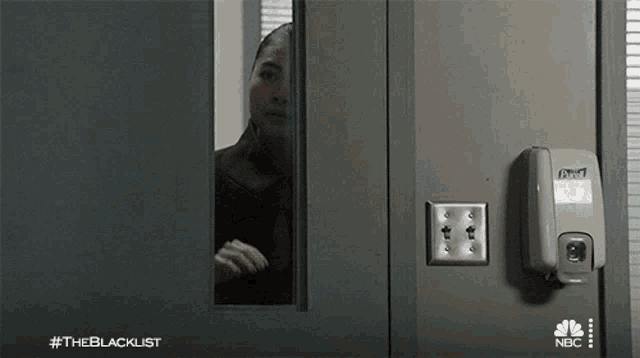 a woman is peeking out of a door with a hand sanitizer dispenser on it