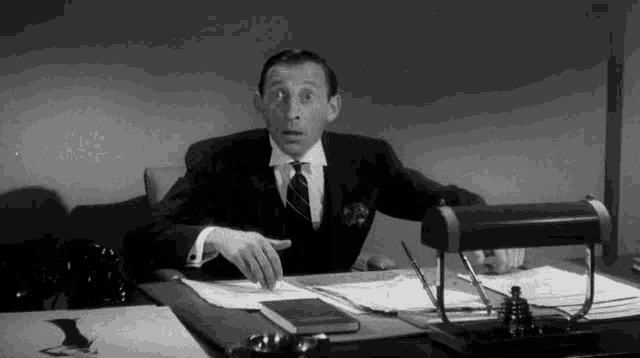 a man in a suit and tie is sitting at a desk with papers on it .