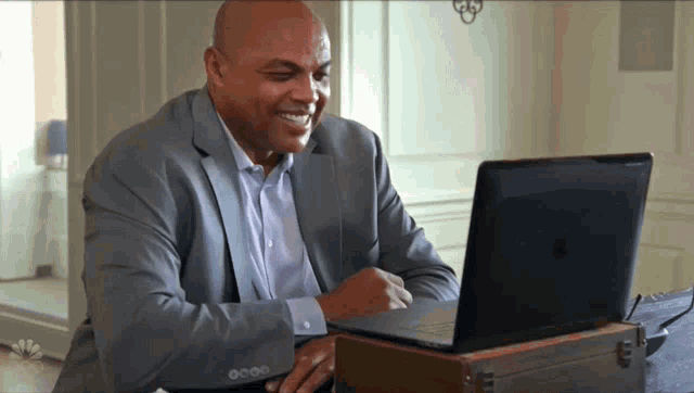 a man in a suit is smiling while using a laptop computer