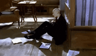 a bald man in a suit sits on the floor with papers on the floor