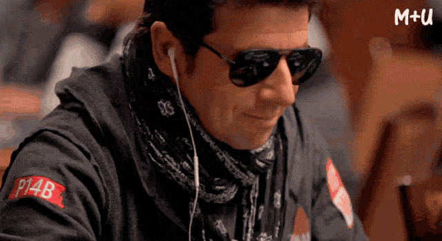 a man wearing sunglasses and ear buds has a shirt that says m + u on it