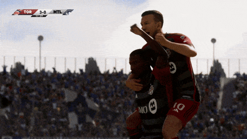 two soccer players are celebrating a goal in front of a crowd with the score 3-0