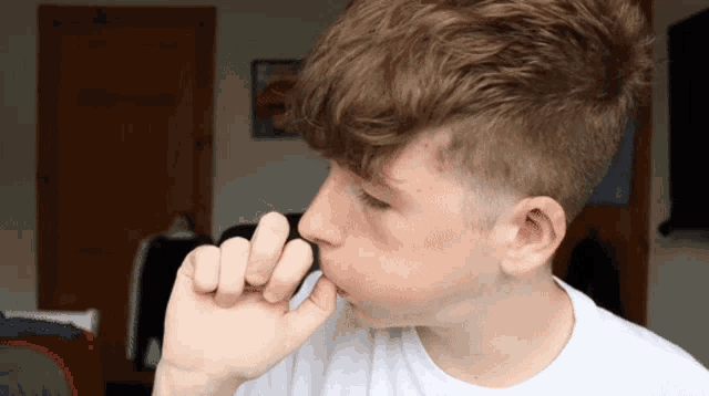 a young boy with a white shirt is holding his hand to his face