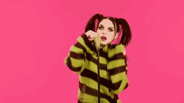 a woman in a green and black striped sweater is singing into a microphone