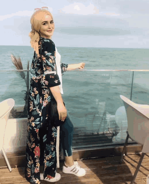 a woman standing on a balcony overlooking the ocean wearing a floral cardigan