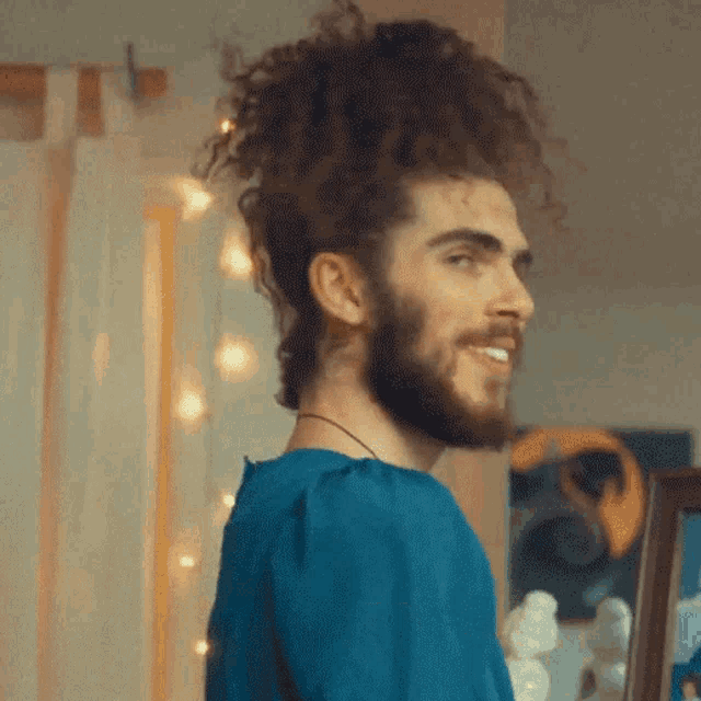 a man with curly hair and a beard is wearing a blue shirt and smiling