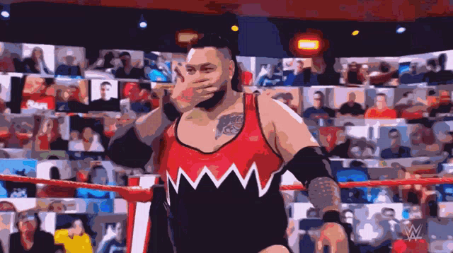 a wrestler covering his face with his hand in front of a crowd that says raw
