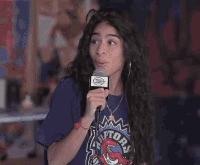 a woman wearing a raptors shirt is holding a microphone .