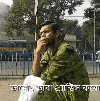 a man with a beard is sitting in front of a fence with a bus in the background ..