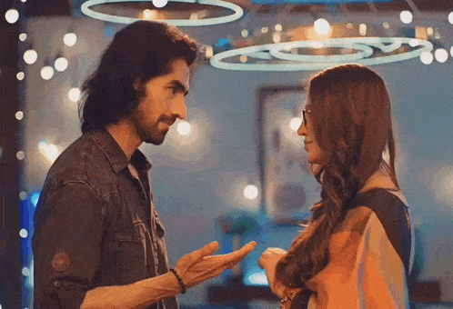 a man and a woman are looking at each other in a room with lights hanging from the ceiling .