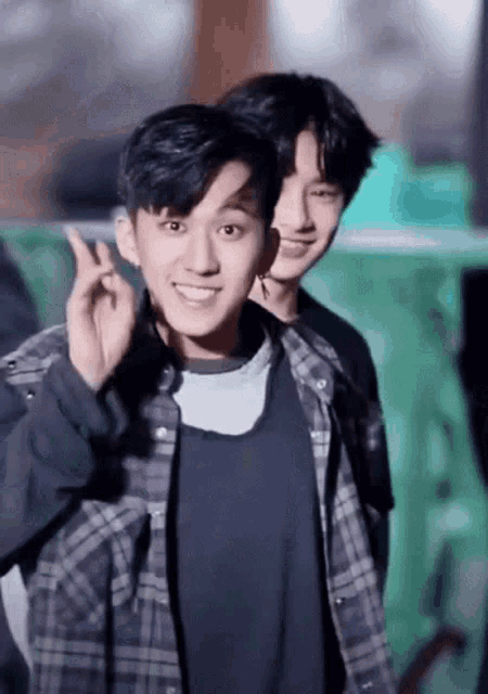 two young men are standing next to each other and one of them is making a heart sign .