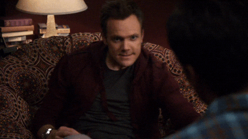 a man sitting on a couch is pointing at another man with the words watch it behind him