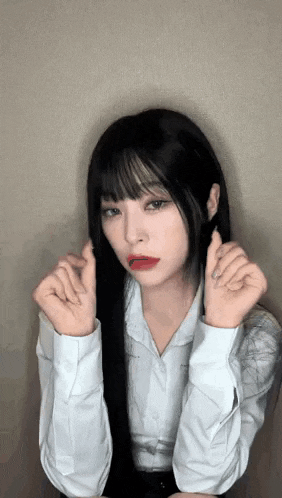 a woman with long black hair and red lips is making a heart shape with her hands .