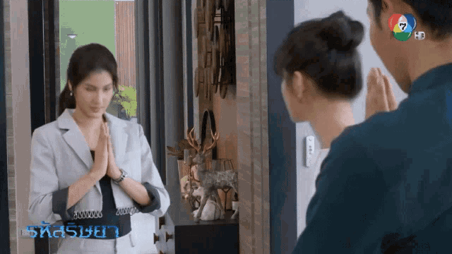 a woman in a suit is praying in front of a mirror while a man looks on ..