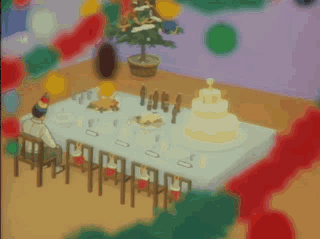 a man in a party hat sits at a table with a cake and a christmas tree in the background