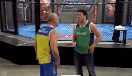 two men are standing in front of a cage with the word fighter on the wall behind them