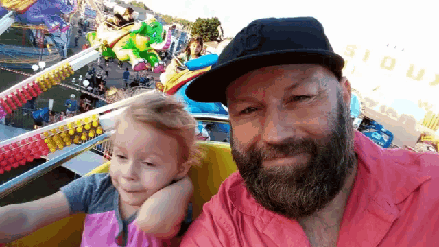 a man with a beard is holding a little girl on a roller coaster at a carnival