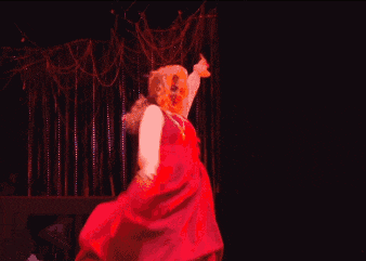 a woman in a red dress is dancing on a stage with her arms outstretched