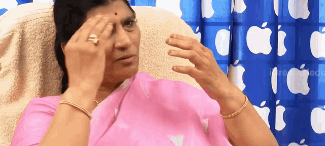 a woman in a pink saree is sitting in front of a blue curtain with apples on it