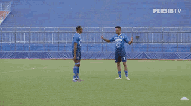 two soccer players shake hands on a field with a persibtv logo behind them