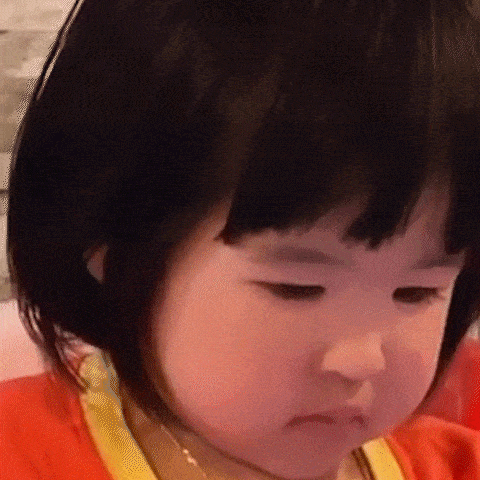 a little girl with short black hair is making a funny face while wearing a red shirt .