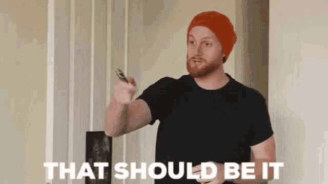 a man with a beard wearing an orange hat is pointing at something with the words that should be it behind him .
