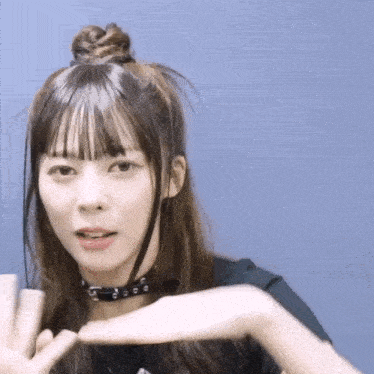 a woman wearing a choker and a bun is making a heart shape with her hands