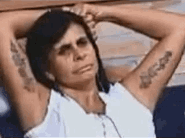 a woman with a tattoo on her arm is sitting on a bench with her hands behind her head .