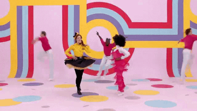 a group of people are dancing in front of a pink wall with colorful lines .