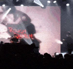 a man playing drums in front of a large screen that says rough rider on it