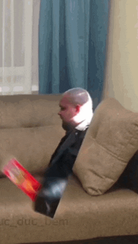 a man with a bandage on his head is sitting on a couch eating chips