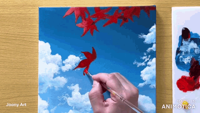 a person is painting a maple leaf with a brush on a canvas