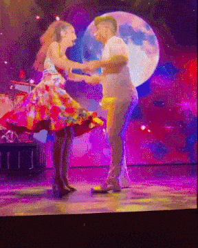 a man and a woman are dancing on a stage with a full moon behind them
