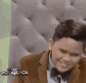 a young man in a suit and bow tie is smiling while sitting on a couch .