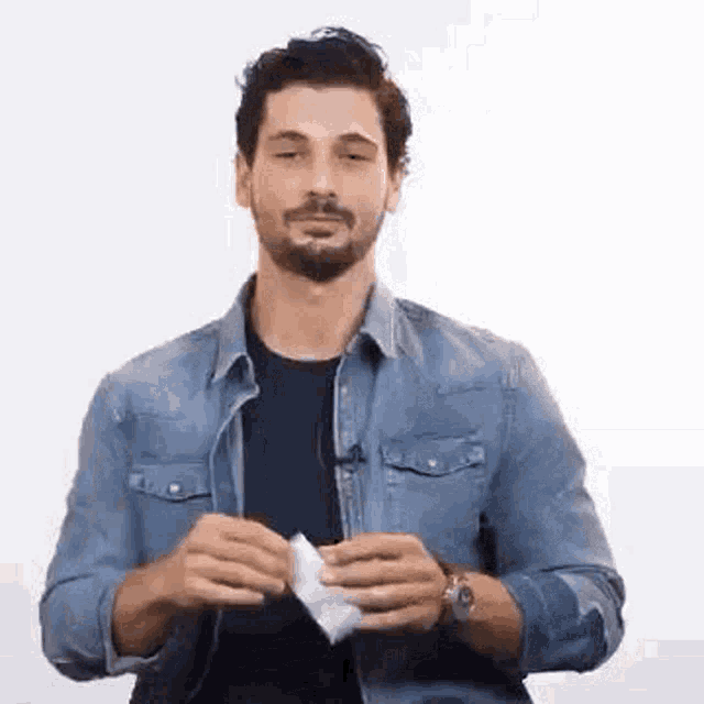 a man with a beard is wearing a denim shirt and holding a piece of paper in his hands .