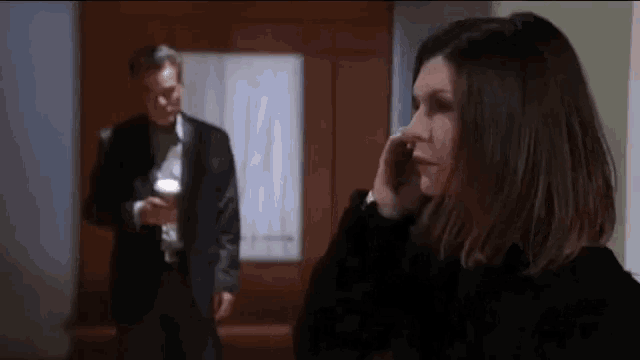 a woman is talking on a cell phone while a man stands behind her .
