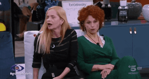 two women sit on a couch with a sign that says brosway in the background