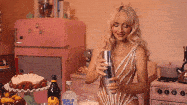 a woman in a bathing suit is shaking a drink in a kitchen with a bottle of absolut vodka behind her