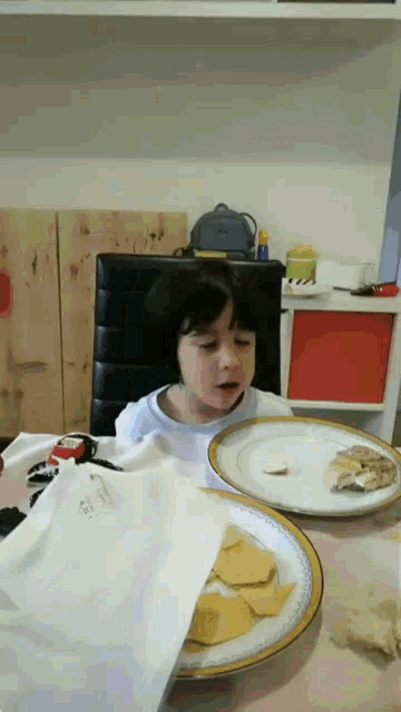 a little girl sits at a table with plates of food