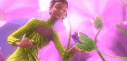 a woman in a green dress is holding a purple flower in her hand .